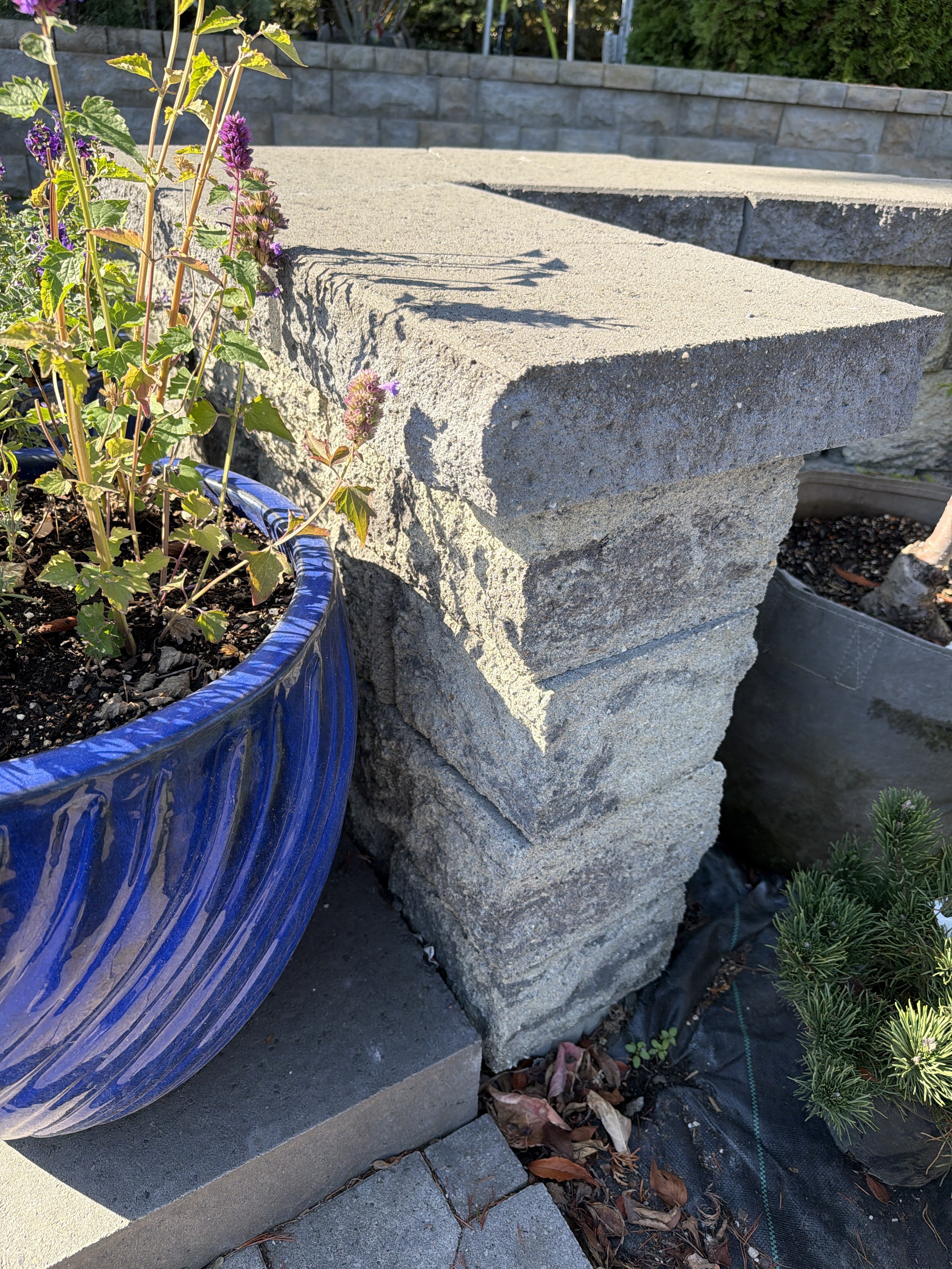 Close view of a textured cap extending over the exposed end of a block wall beside a blue planter.