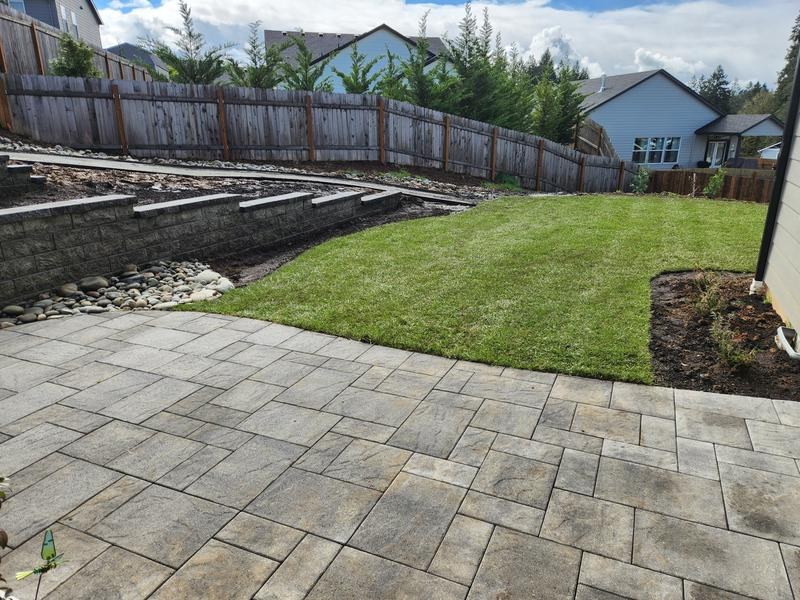 A natural grass lawn beside a paver patio and retaining wall.