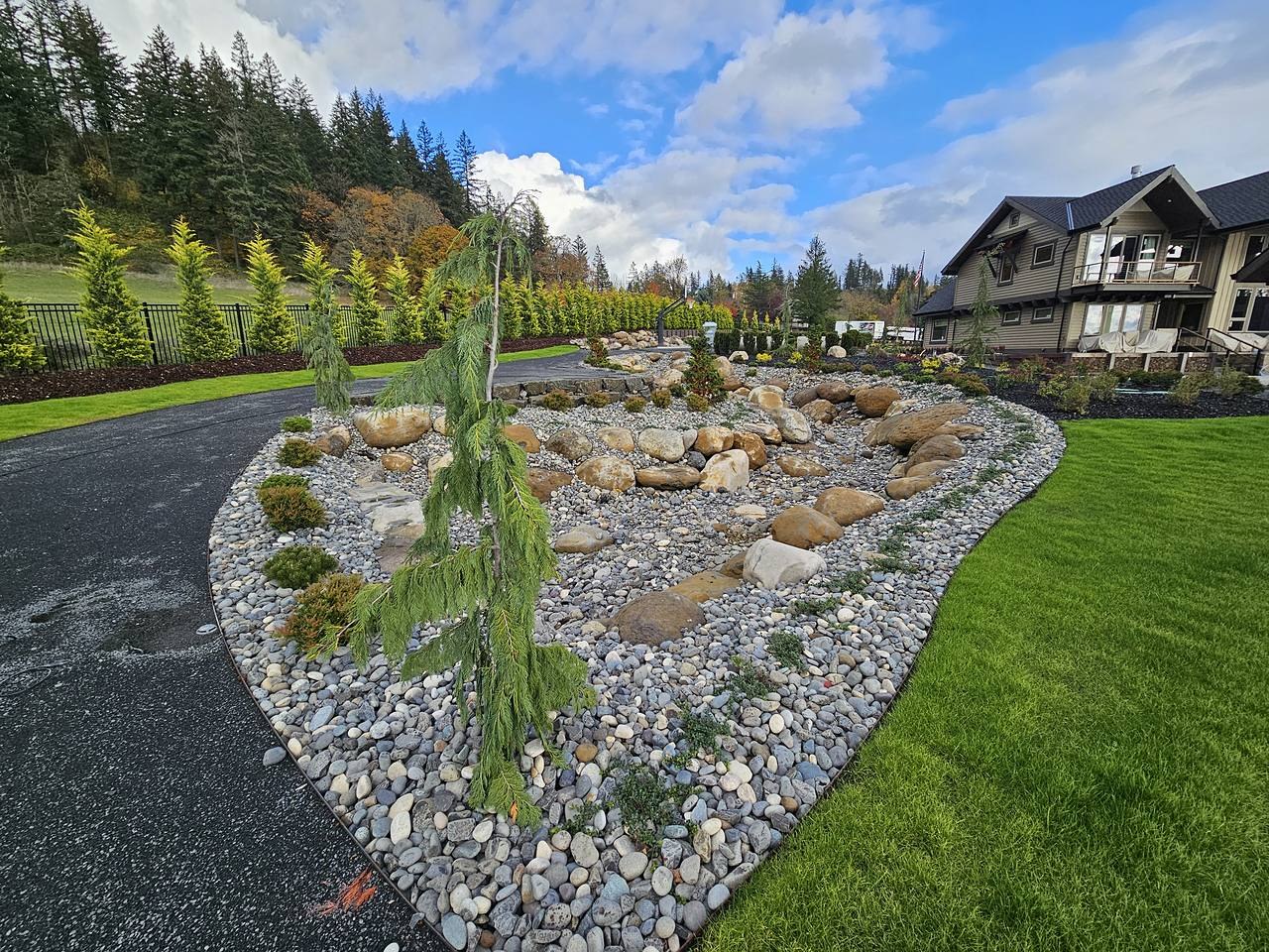 A residential landscape with stone-covered planting beds, boulders and darker mulched borders.